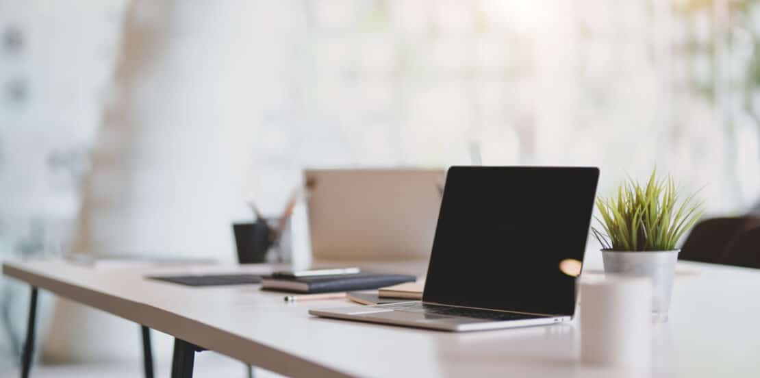 Open blank laptop in modern workplace with office supplies and decorations on white table
