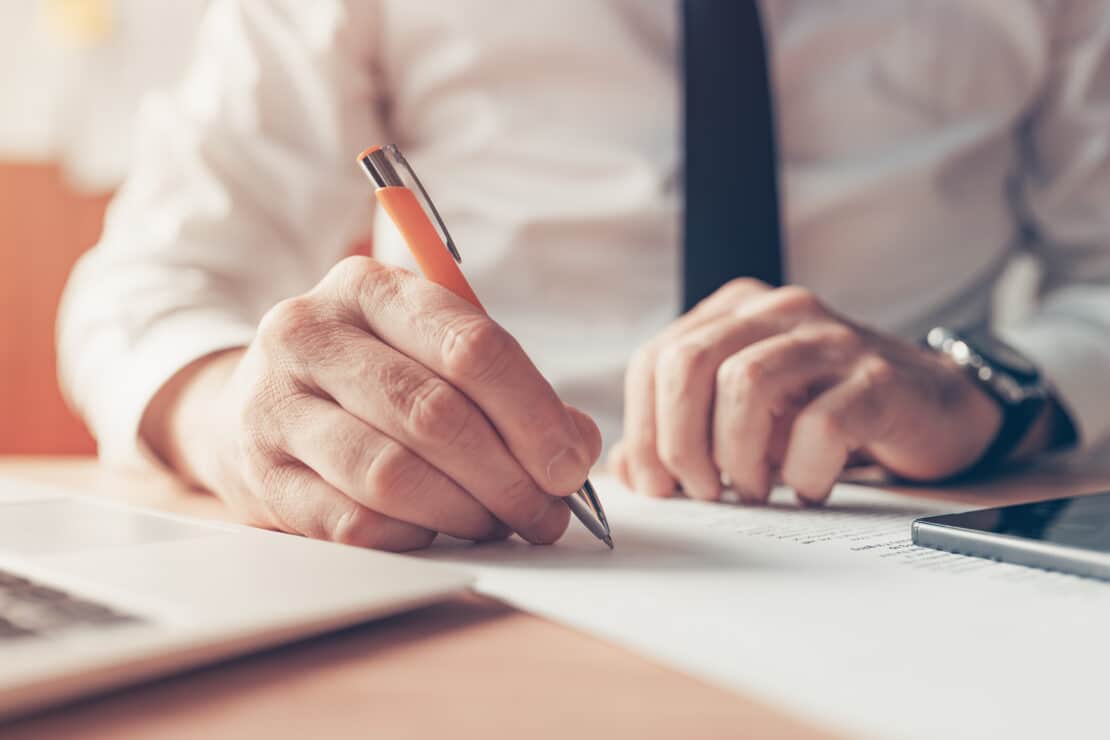 Businessman writing notes at office desk, close up with selective focus