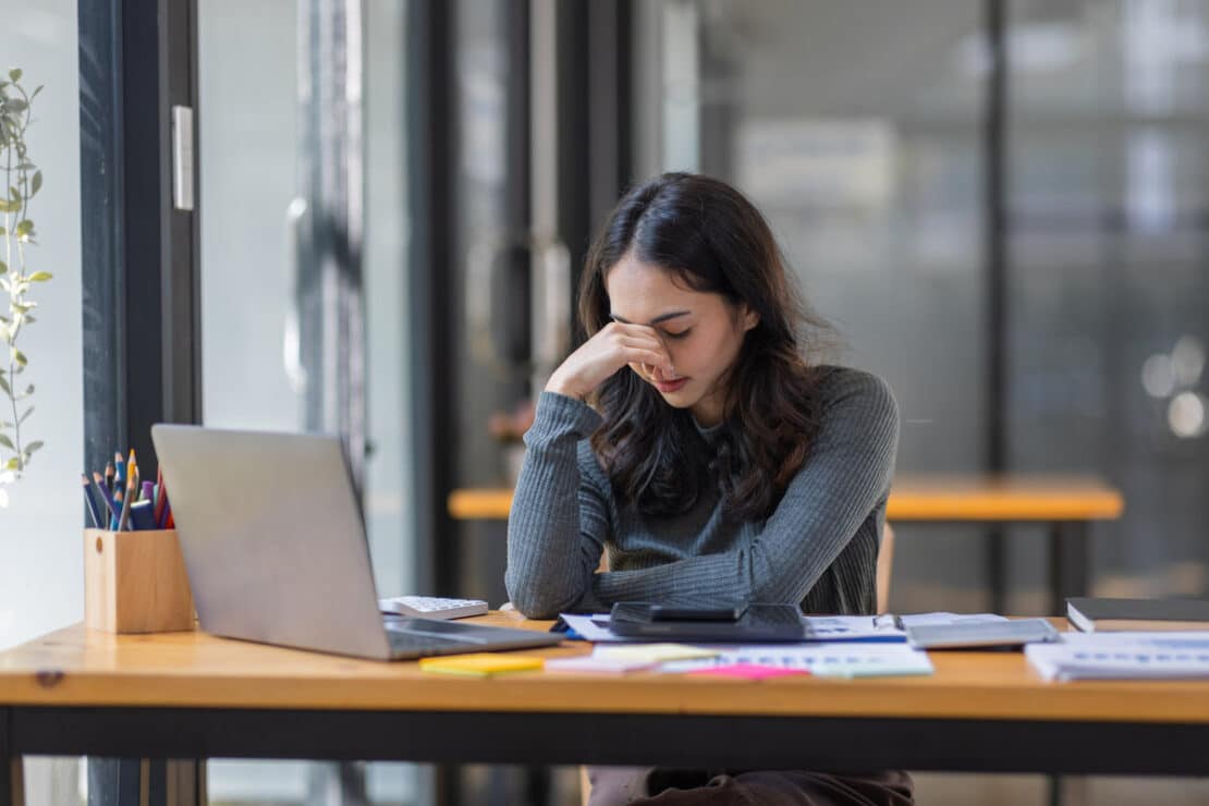 Portrait of tired young business Asian woman work with documents tax laptop computer in office. Sad, unhappy, Worried, Depression, or employee life stress concept